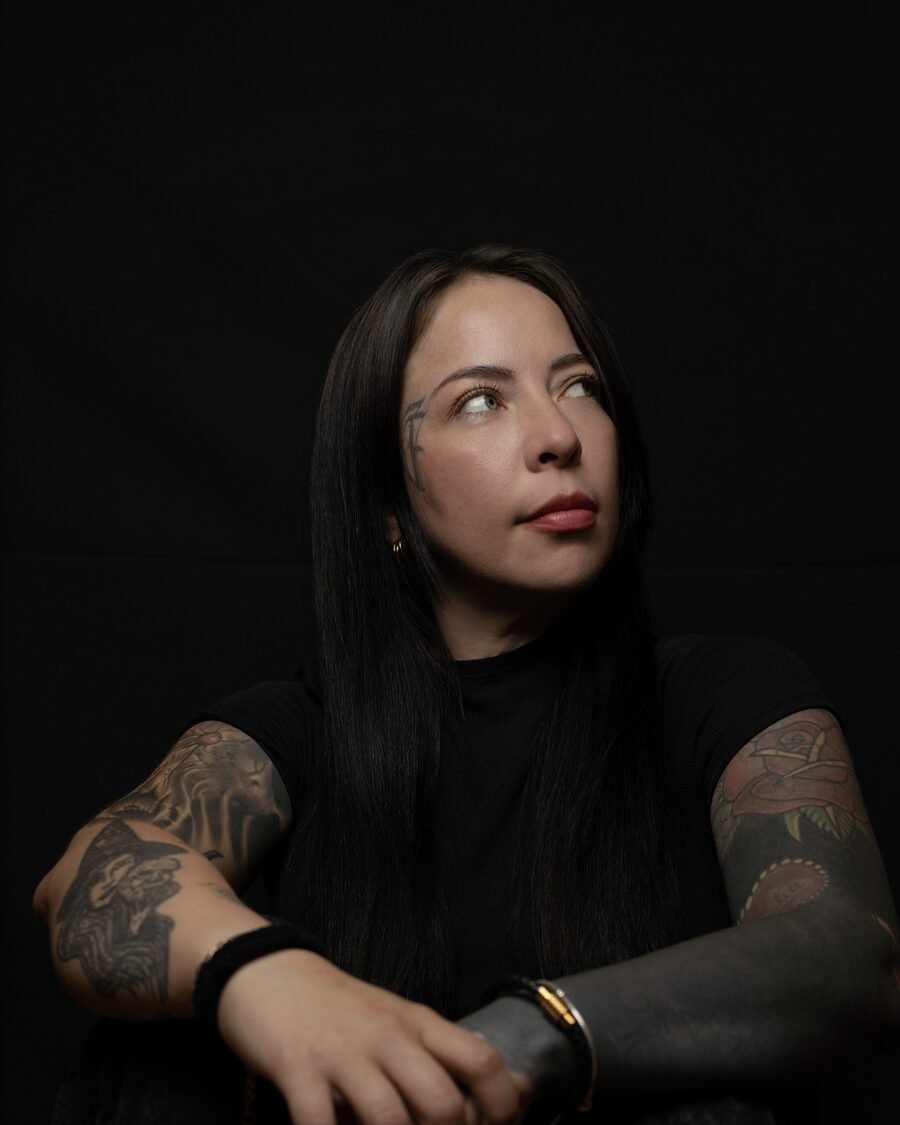 Retrato de Catherine Armas sobre fondo negro, vestida de negro, con los brazos tatuados cruzados
